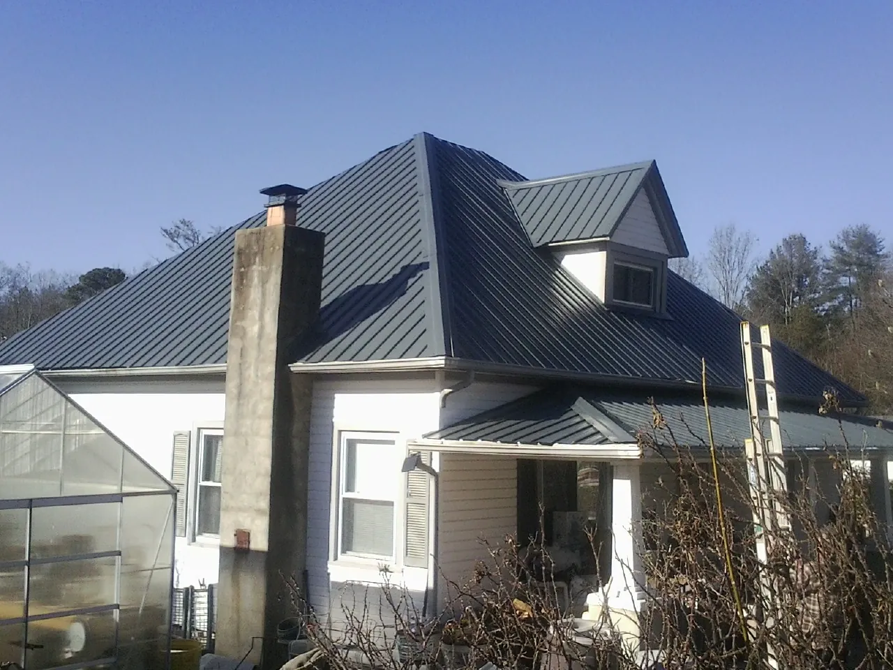 Dark blue standing seam metal roof on a white farmhouse with dormer in Landenberg
