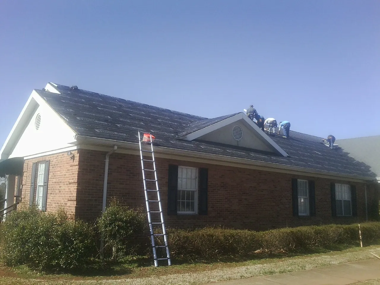 Crew tearing shingles off a brick ranch roof with a ladder set — Metal Roof Repair work by our crew in Landenberg
