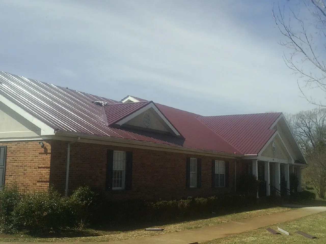 Red metal roof with gabled entries on a long brick building, from a Hail Damage Roof Repair job in Landenberg