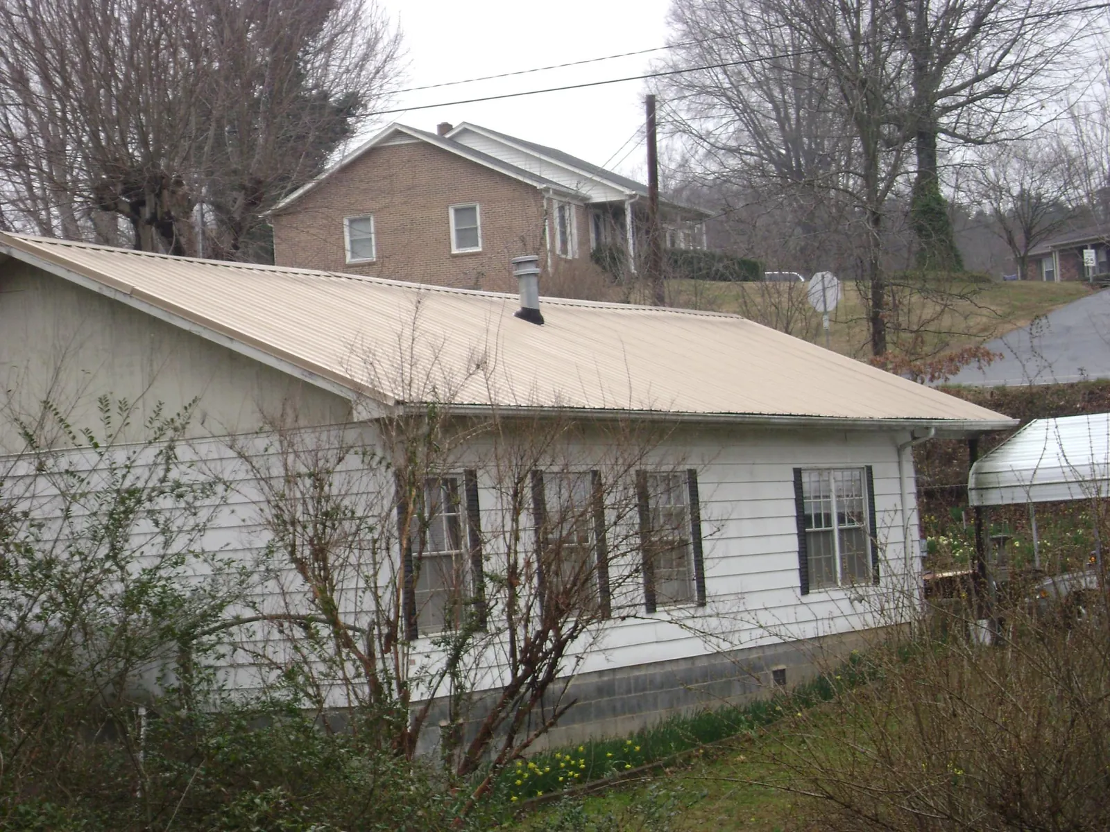 Tan metal roof on a white sided house set into a hillside — Commercial Roofing by Roofing Brothers in Landenberg